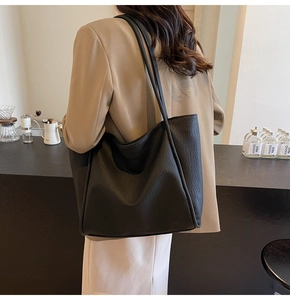 Lifestyle shot of large black pebble leather tote bag worn by a model in a beige suit