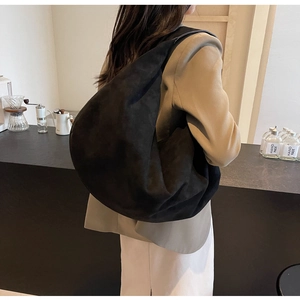 Chic oversized black suede crescent bag worn by model in a warm cafe setting