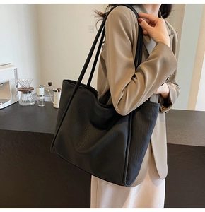 Close-up of a large black textured leather tote bag with slim shoulder straps for daily commute