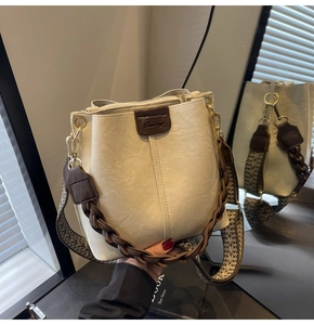 Detail of cream bucket bag showing woven handle, patterned strap, and leather logo patch