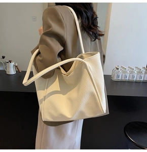 Detail of a creamy white tote bag with lychee grain leather texture on a female shoulder