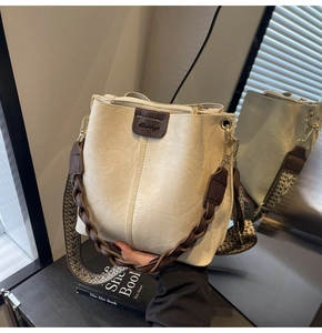 Detail of white bucket bag with brown leather trim and woven shoulder strap on book