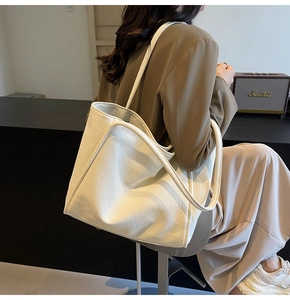 Detailed side view of off-white textured leather tote bag worn on a woman's shoulder