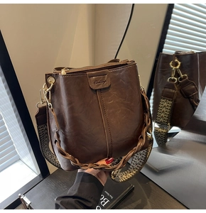 Detail of dark brown leather bucket bag with woven handle and geometric wide strap
