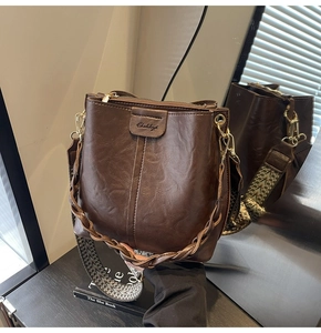 Detail of dark brown bucket bag with wide geometric strap and golden hardware accents