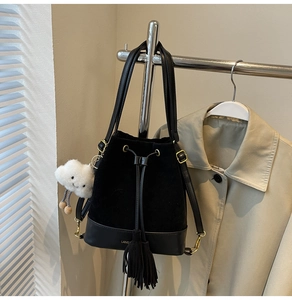 Detail of black drawstring bucket bag with tassel and plush charm on a metal hanger