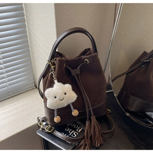 Detail of dark brown drawstring bucket bag featuring a plush charm and tassel accents