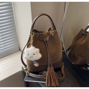 Detail of brown suede bucket bag featuring leather drawstring tassels and plush charm