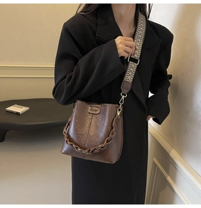 Close-up of retro brown bucket bag featuring woven handle and wide geometric textile strap