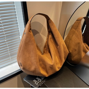 Detail of caramel suede hobo bag with wide shoulder strap and metal rivets in a studio