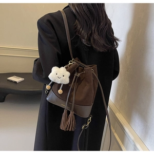 Detail of dark brown suede bucket bag with tassels and plush cloud charm on a model