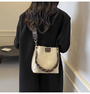 Beige leather bucket bag with retro patterned wide strap and woven handle on model