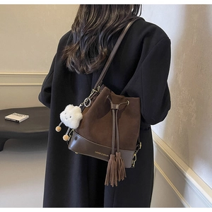 Detail of a brown suede bucket bag with long tassels and a white cloud plush pendant