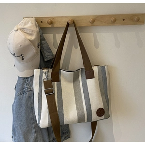 Detailed view of striped canvas tote bag with brown straps hanging on a wooden rack