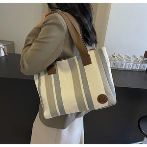 Detail of striped canvas tote bag with brown shoulder strap and leather logo patch