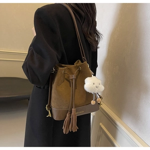 Close-up of retro brown bucket bag featuring leather tassels and a plush cloud charm