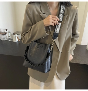 Detail of black bucket bag featuring textured wide strap and chunky chain decoration