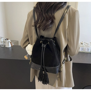 Detail of black drawstring bucket backpack with tassels and plush charm on a model