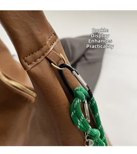 Detail of brown faux leather bag featuring black D-ring buckle and green braided rope