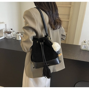 Detail of a vintage black bucket bag with fringe tassels and a white plush keychain