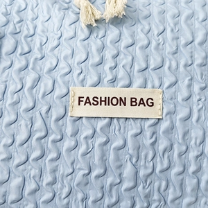 Close-up of light blue bubble-textured fabric with white fashion bag label and fringe