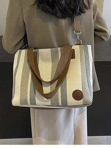 Minimalist striped canvas tote bag with brown straps worn by a model in a trench coat