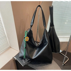 Detail of black faux leather tote bag featuring green braided rope and smiley face charm