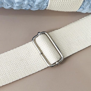 Detail of light blue textured fabric with off-white canvas strap and silver buckle