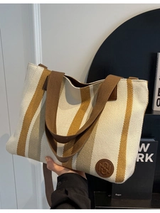Large striped canvas tote bag with brown handles and leather logo patch in casual style