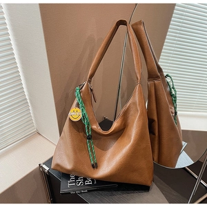 Detail of a brown Hobo tote bag featuring a green woven rope and smiley charm