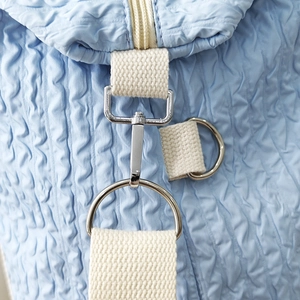 Close-up of light blue quilted travel bag showing silver metal hooks and wave texture