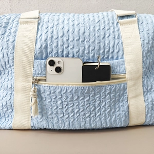 Close-up of the front zipper pocket holding a smartphone in a sky blue travel bag