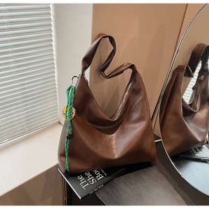 Detail of caramel brown tote bag featuring crackled faux leather and woven rope charm