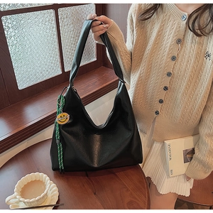 Detailed macro of large black hobo tote bag featuring a green rope and yellow smiley charm