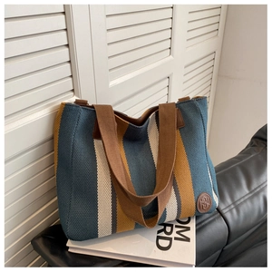 Detail of striped canvas tote bag with brown leather logo patch and nylon strap