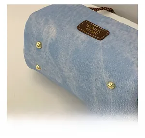 Detail view of denim bag bottom featuring four protective gold metal studs and brand patch