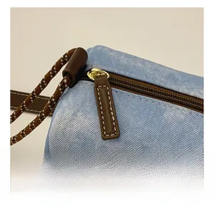Detail showing blue denim texture, smooth golden zipper, and woven brown strap on bag