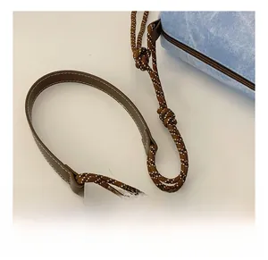 Close-up of woven shoulder strap with leather pad on blue denim underarm bag