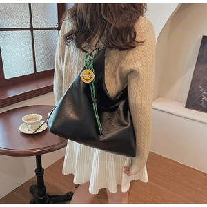 Detail of a black large capacity tote bag with green rope and smiley face charm