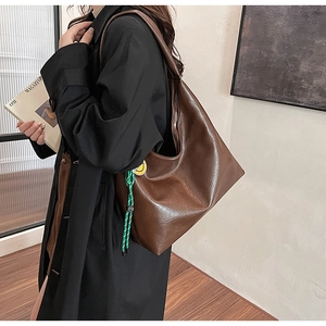Close-up of brown leather tote bag with colorful braided rope and yellow smiley badge detail