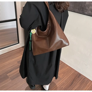 Detail of a large brown faux leather tote bag featuring a green woven rope and smiley charm