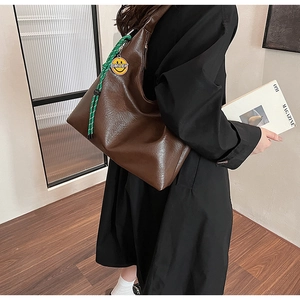 Detail of dark brown leather hobo bag with a green rope charm and smiley badge detail