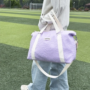 Outdoor shot of light purple quilted duffle bag with white handles on green grass