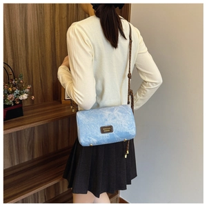Detail shot of light blue textured fabric shoulder bag with leather logo and brown strap