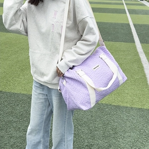 Close-up of light purple quilted travel bag with reinforced white handles and shoulder strap