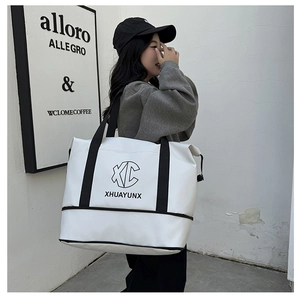 Close-up of a white travel tote bag with black XC logo being carried by a model