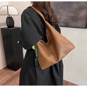 Close-up of caramel brown leather tote bag with a smile charm and green woven pendant