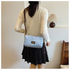 Detail of light blue pillow bag showing woven shoulder strap and golden metal bottom studs