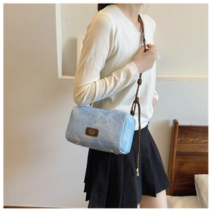 Detail of light blue textured shoulder bag with woven rope strap and gold hardware