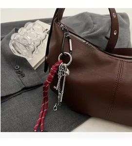 Detail of dark brown leather handbag with red braided keychain on grey blazer backdrop